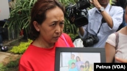 Nana Fariawati kerabat Penumpang Pesawat Air Asia QZ8501 menunjukkan foto empat orang anggota keluarga yang menjadi penumpang pesawat yang hilang, Senin, 29 Desember 2014 (Foto: VOA/Petrus).