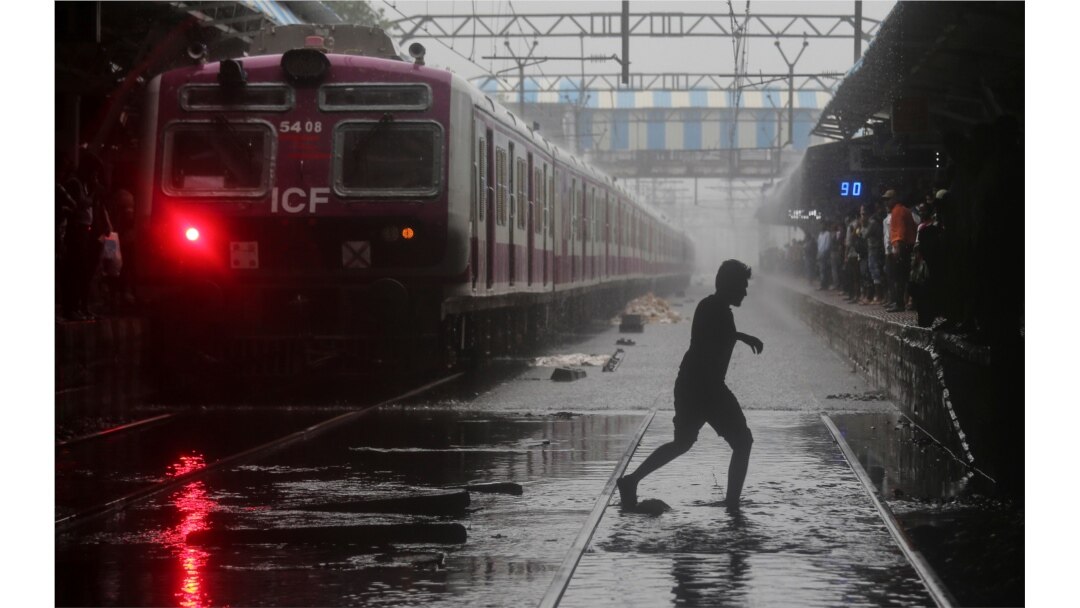 Seorang komuter melintasi rel kereta api yang tergenang air di Mumbai, India, 2 Juli 2019. (Foto: Reuters / Francis Mascarenhas)