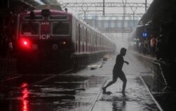 Seorang komuter melintasi rel kereta api yang tergenang air di Mumbai, India, 2 Juli 2019. (Foto: Reuters / Francis Mascarenhas)