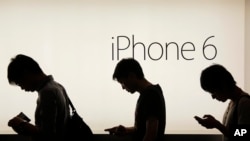 In this file photo, people wait to buy the Apple iPhone 6 and 6 Plus devices outside an Apple store in Hong Kong, Sept. 19, 2014.