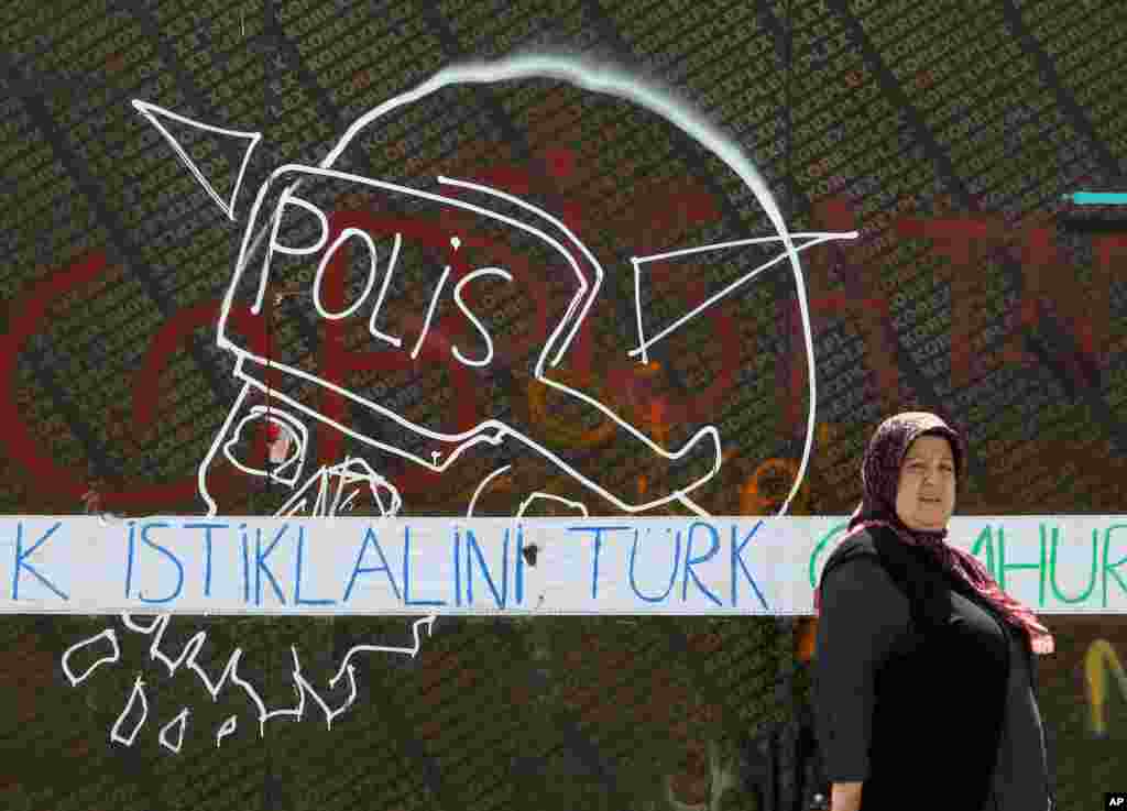 A woman passes next to a graffiti with a police helmet as the blue words reading ''Turk independence'' at Taksim Square, Istanbul, June 3, 2013. 