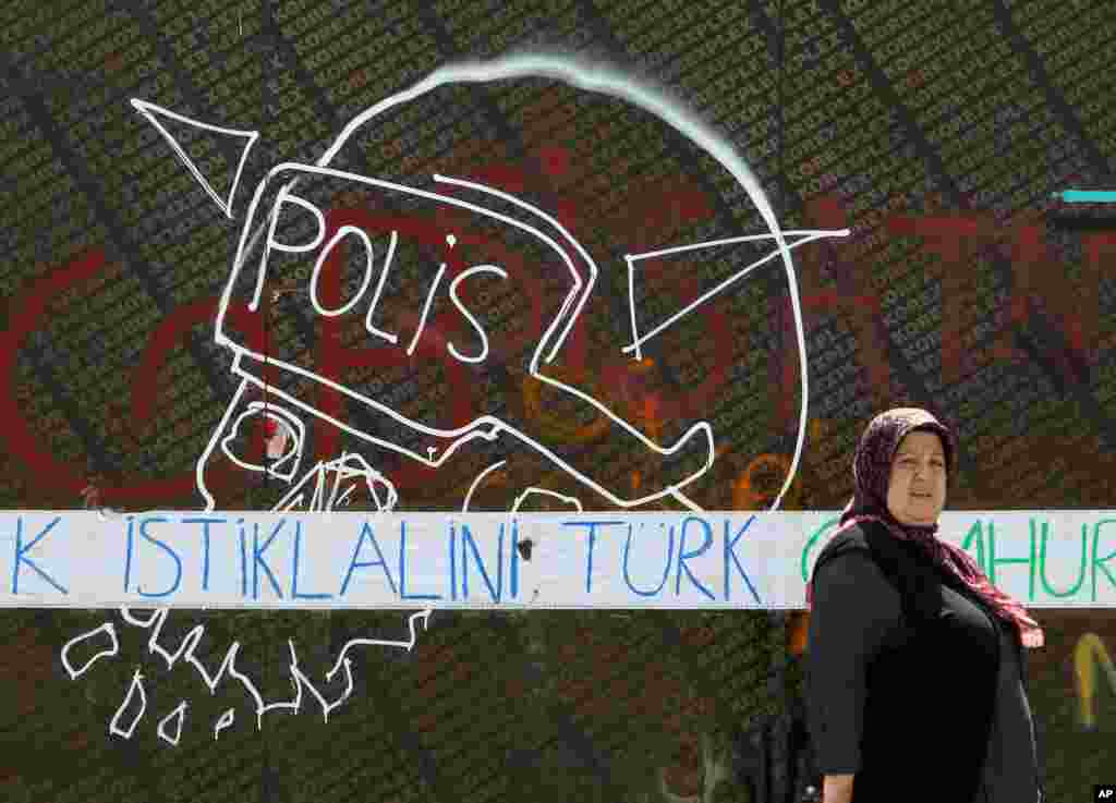 A woman passes next to a graffiti with a police helmet as the blue words reading ''Turk independence'' at Taksim Square, Istanbul, June 3, 2013.