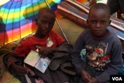 Children shield themselves from the morning sun at a reception camp in Eastern Rwanda, while they wait to be sent to one of the refugee camps set by the Rwandan government. (Mohammed Yusuf for VOA)