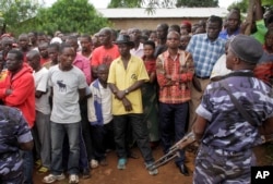 FILE - Policemen stand guard as residents gather at the scene where more than 20 people were killed in their homes in an overnight attack in the Ruhagarika community of the rural northwestern province of Cibitoke, in Burundi, May 12, 2018.