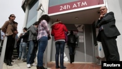 People queue up to make a transaction at an ATM outside a branch of Laiki Bank in Nicosia, March 21, 2013. 