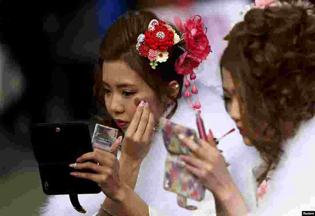 Mulheres japonesas vestidas de kimonos maquilham-se para a cerimónia do Coming of Age Day num parque de diversões de Tóquio.&nbsp;
