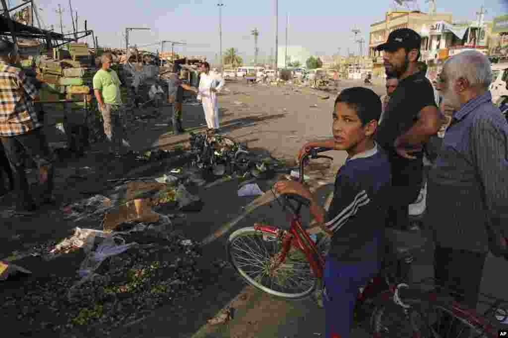 Iraqi civilians gather the morning after a car bomb killed many people and wounded tens of others in a crowded outdoor market, in the Shiite neighborhood known as Sadr City, Baghad Iraq, July 16, 2014.