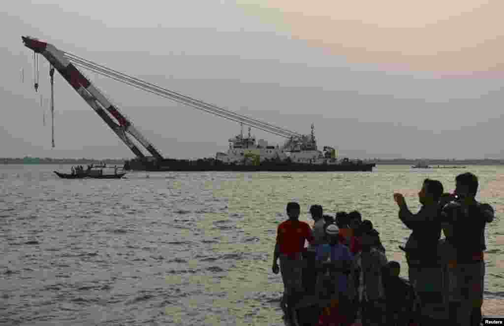 People watch and take pictures as a rescue vessel tries to provide help to the ferry that capsized in the Meghna river, Munshiganj, Bangladesh, May 15, 2014. 