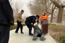 FILE - An officer helps up a drunk man passed out by a trash bin in Poksam County, in northwestern China's Xinjiang Uyghur Autonomous Region, March 21, 2021.