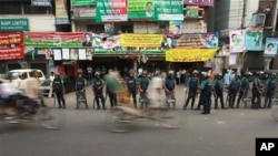Bangladeshi rickshaw pullers pedal past riot police standing guard in front of the main opposition Bangladesh Nationalist Party (BNP) office in Dhaka, Bangladesh, 29 Nov., 2010.