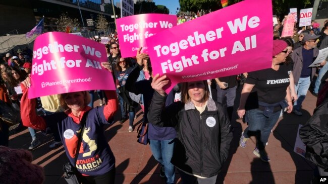FILE - People carrying signs join hundreds of demonstrators in the Women's March in downtown Los Angeles, Jan. 20, 2018.