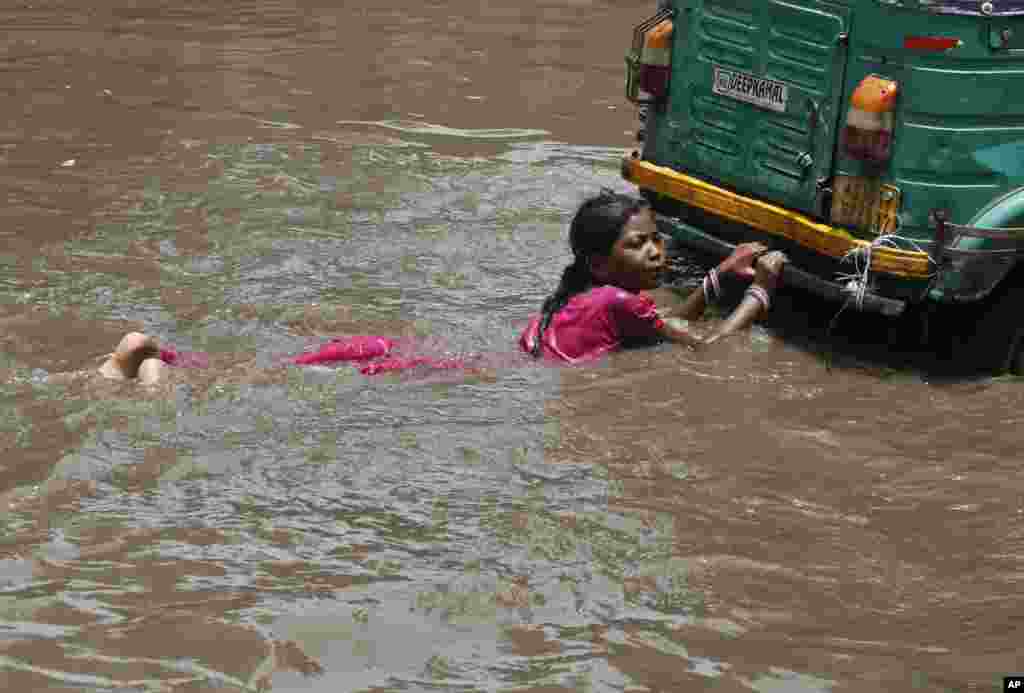 An Indian girl holds on to the back of an auto-rickshaw as she plays in a flooded street with other children after a heavy monsoon rain in Ahmadabad, India.