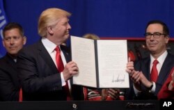 President Donald Trump, accompanied by Treasury Secretary Steven Mnuchin, right, and others, holds up an executive order he signed during a visit to the headquarters of tool manufacturer Snap-on Inc. in Kenosha, Wis., Tuesday, April 18, 2017.