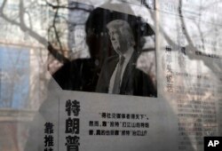 FILE - A man reading a newspaper posted on a public newspaper bulletin board is reflected on a glass as a photo of U.S. President-elect Donald Trump is published on a Chinese newspaper with an article that reads "Trump uses fist to talk" in Beijing, Jan. 3, 2017.