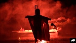 People on a boat hold flares as they sail behind the effigy of Judas during the revival of the old Easter tradition of the "burning of the Judas", in the port town of Ermioni, in the Peloponnese peninsula, southwest of Athens, April 8, 2018. 