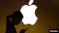 FILE - A woman looks at the screen of her mobile phone in front of an Apple logo outside its store in downtown Shanghai, Sept. 10, 2013.