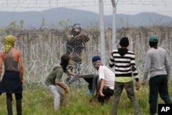 FILE - Migrant men trying to remove barbed wire along the fence clash with Macedonian police at the northern Greek border point of Idomeni, Greece, April 13, 2016.