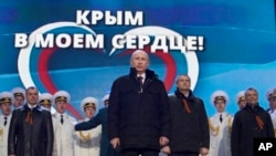 Russian President Vladimir Putin, with leaders of newly-annexed Crimea in the background, is seen at a rally in Moscow, March 18, 2014. The sign in the back reads "Crimea is in my heart!"