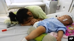 Nine-month-old boy Dao Xuan T, from the southern province of Binh Duong and affected by hand, foot and mouth disease, lies on a bed next to his sleeping mother at a local pediatric hospital in the southern province of Dong Nai, FILE August 24, 2011.