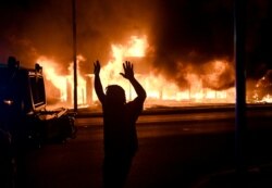 A man walks by an armoured vehicle as B&L Office Furniture burns in the background as protests turn to fires after a Black man, identified as Jacob Blake, was shot several times by police last night in Kenosha, Wisconsin, U.S. August 24, 2020.