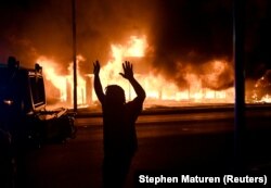 A man walks by an armoured vehicle as B&L Office Furniture burns in the background as protests turn to fires after a Black man, identified as Jacob Blake, was shot several times by police last night in Kenosha, Wisconsin, U.S. August 24, 2020.