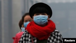 FILE - Women wearing masks make their way amid the heavy haze in Beijing, Feb. 23, 2014.