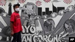 A man wearing face mask walks past a coronavirus-themed mural in Jakarta, Indonesia, Wednesday, Nov. 25, 2020. Writings on the mural read "Let's fight coronavirus." (AP Photo/Tatan Syuflana)