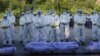 TOPSHOT - Volunteers wearing personal protective equipment (PPE) pray in front of bodies of people who died from the Covid-19 coronavirus during their funeral at a cemetery in Mandalay on July 14, 2021. (Photo by STR / AFP)