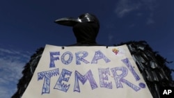 A demonstrator dressed in a black feathered costume holds a sign stating Brazil's President Michel Temer should "get out," during an anti-government protest in Brasilia, May 24, 2017. 