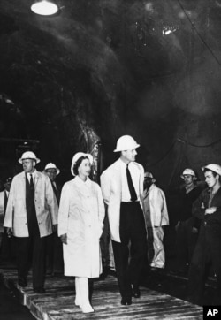 FILE - Queen Elizabeth II and her husband, Prince Philip, walk through the Gieehi Dam tunnel, part of a $320 million hydroelectric and irrigation scheme, inspecting work on the Snowy Mountain project at Cabrumurra, New South Wales, March 9, 1963.