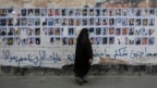 FILE - A Bahraini woman walks past images of political prisoners plastered on a wall in Sanabis, Bahrain, Oct. 22, 2015. In May 2018, the court revoked the citizenship of 115 people in a mass terrorism trial.