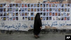 FILE - A Bahraini woman walks past images of political prisoners plastered on a wall in Sanabis, Bahrain, Oct. 22, 2015. In May 2018, the court revoked the citizenship of 115 people in a mass terrorism trial.