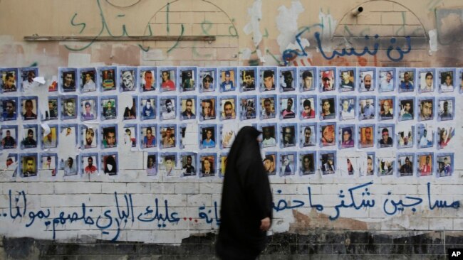 一名巴林妇女站在贴满政治犯图片的墙壁前