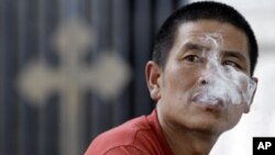 A man blows out cigarette smoke outside a church in Beijing August 18, 2010. Only a quarter of Chinese people believe smoking tobacco increases the risk of cancer and anti-smoking campaigns are failing to influence them, a government survey released on Tu