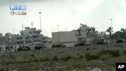 This image made from amateur video and released by Shams News Network and accessed via The Associated Press Television News on Saturday, Aug. 13, 2011, shows a long shot of military vehicles lined up on road, backdrop of buildings taking up positions near