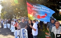 FILE - Supporters of the Alternative for Germany party hold signs reading "Merkel must go" and a flag reading "Our country, our homeland," as they protest during a campaign event of German Chancellor Angela Merkel in Bitterfeld, eastern Germany, Aug. 29, 2017.