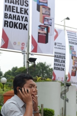 Seorang pria merokok di sebelah spanduk bertuliskan "harus waspada akan bahaya merokok" di Jakarta. (Foto: AFP/Adek Berry)