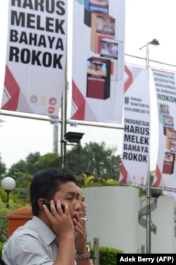 ILUSTRSI - Seorang pria merokok di sebelah spanduk bertuliskan "harus waspada akan bahaya merokok" di Jakarta pada 24 Juni 2014. (Foto: AFP/Adek Berry)