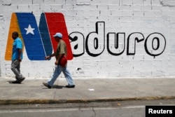 Supporters of Venezuela's President Nicolas Maduro walk past a campaign mural before a rally with him, in Charallave, Venezuela, May 15, 2018.