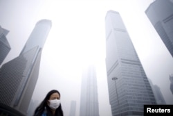 FILE - A woman wearing a mask walks past skyscrapers amid heavy smog in Shanghai, China, Dec. 11, 2015. United Nations Secretary-General Ban Ki-moon said that acting on climate change promises "new markets," along with "better jobs" and "better health."