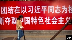 2017年10月12日，一名女子滑著踏板車經過北京街頭的一張標語。（美聯社照片）