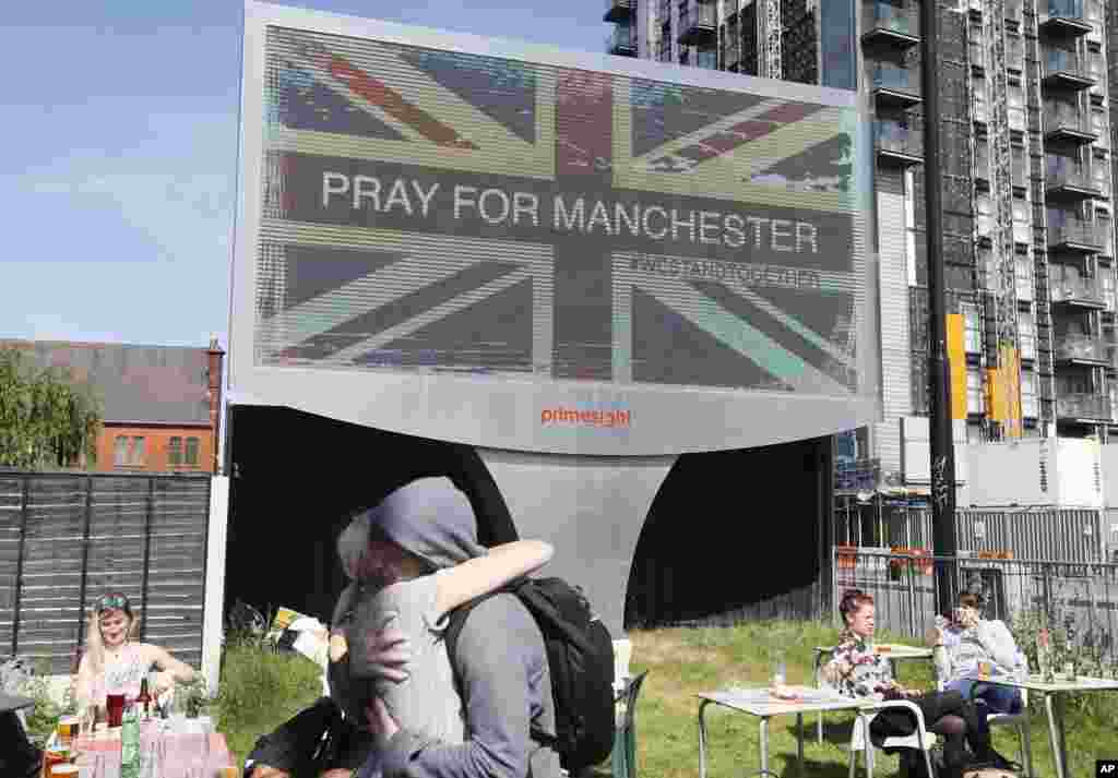 A couple embrace under a billboard in Manchester city center, May 23, 2017, the day after the suicide attack at an Ariana Grande concert that left 22 people dead as it ended on Monday night.