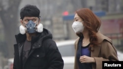 Một cặp đôi đeo mặt nạ ở khu mua sắm trong bối cảnh sương khói nặng sau khi thành phố lần đầu tiên ban hành "báo động đỏ" về tình trạng ô nhiễm không khí tại Bắc Kinh, Trung Quốc, ngày 08 tháng 12 năm 2015. REUTERS / Kim Kyung-Hoon