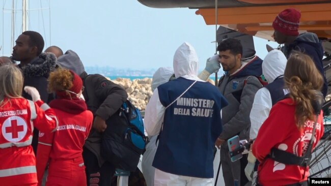 Un funcionario médico con un traje de protección debido al brote de coronavirus, verifica la temperatura de un migrante que desembarca del barco de rescate 'Open Arms' en Pozzallo, Italia, el 2 de febrero de 2020.