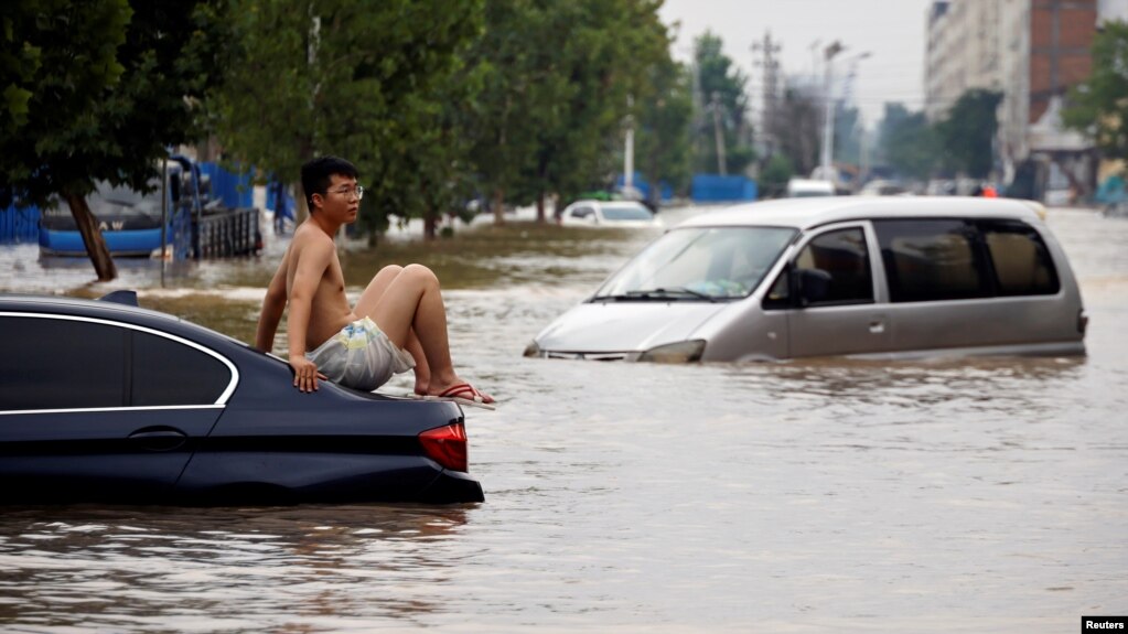 一名男子坐在暴雨后郑州街头漂浮的汽车上。（2021年7月22日）(photo:VOA)