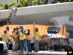 Workers wait near a section of a collapsed pedestrian bridge, March 16, 2018, near Florida International University in the Miami area. The pedestrian bridge, which was under construction, collapsed onto a busy Miami highway Thursday, crushing vehicles beneath it.