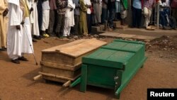 People pray next to caskets containing bodies of two men killed by sectarian violence in Muslim neighborhood of Bangui, March 23, 2014.