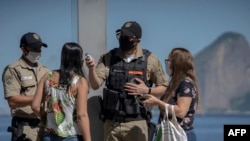 Seorang petugas memeriksa suhu tubuh penumpang yang baru saja turun dari sebuah bis, pada hari pertama pengetatan restriksi karena Covid-19 di Niteroi, Rio de Janeiro, Brazil, 11 Mei 2020. 