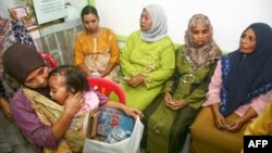 Seorang ibu menggendong anaknya sambil membawa sampah yang dapat didaur ulang di klinik Bumi Ayu, Malang, Jawa Timur. (AFP)