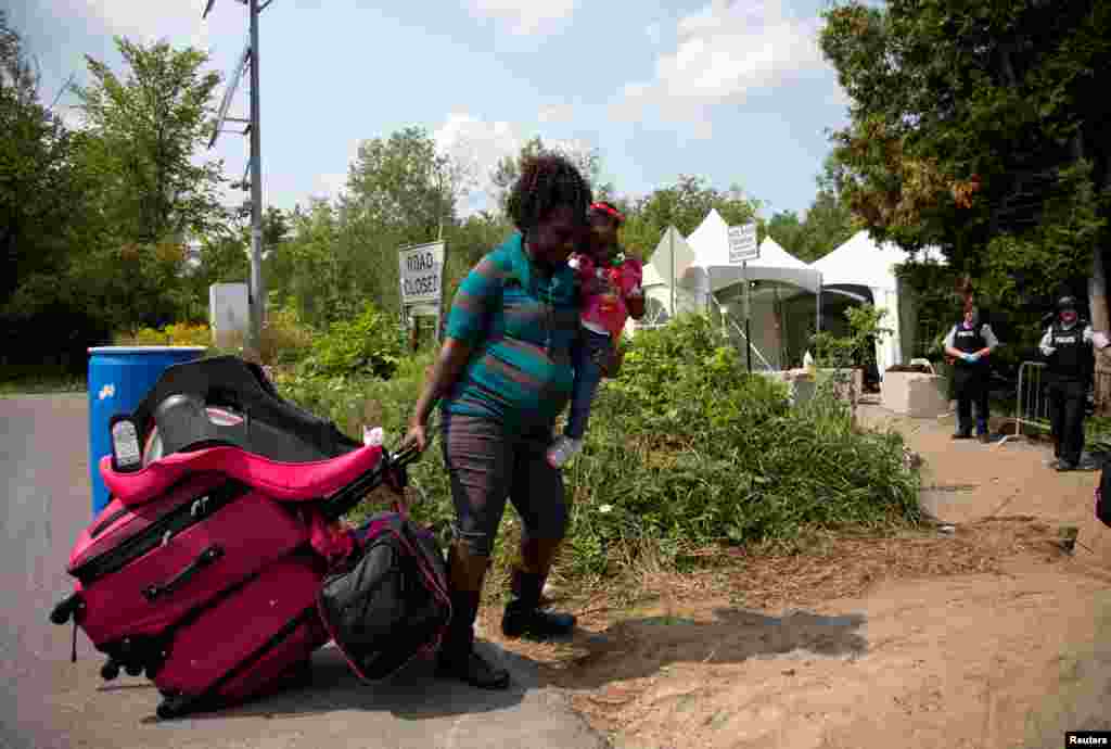 A pregnant mother and her one-and-a-half-year-old daughter Amanda, who stated they were from Haiti, are watched by the Royal Canadian Mounted Police (RCMP) officers as they prepare to cross the U.S.-Canada border into Hemmingford, Quebec, Canada, from Champlain in New York, Aug. 21, 2017.